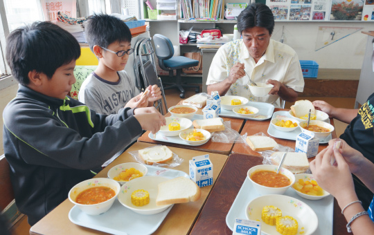 一緒に給食を食べるマンゴー生産者と児童たち